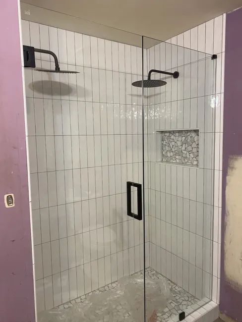2 Panel Frameless Glass Shower with Matte Black Hinges and Handle. The door swings out from the left side and the right side is a fixed panel.