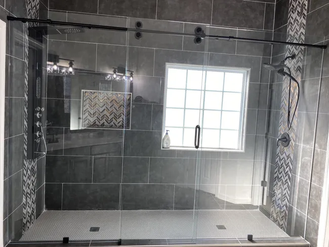 Gorgeous 3 Panel Frameless Sliding Glass Shower Enclosure with Matte Black Hardware and Slider - The door in the middle slides one way and the other two panels are stationary 